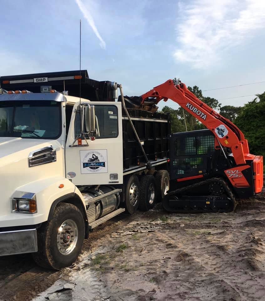 Harrack dump truck and an orange Kubota track loader on a cleared sandy site